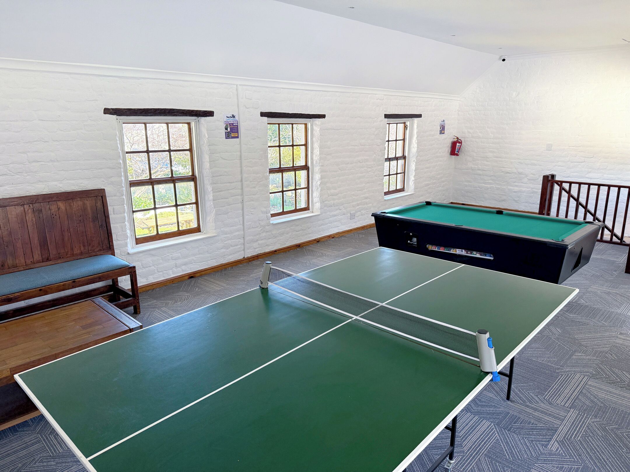 A billiards room with a pool table, benches, and windows.