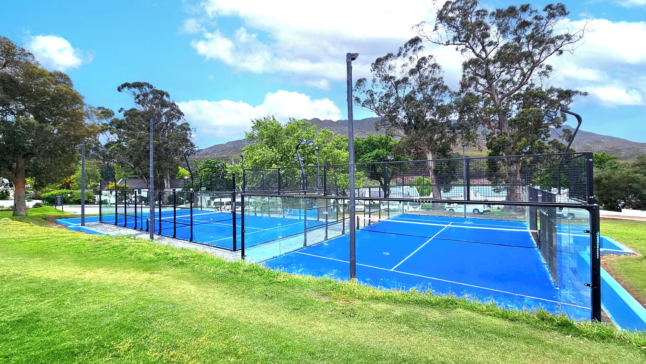 Una cancha de tenis exterior con red, rodeada por una cerca y árboles.