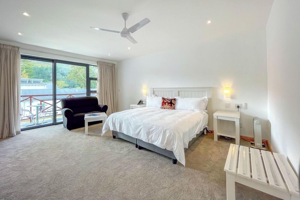 A modern hotel room with a large bed, a ceiling fan, a view of the outdoors, and a small table.