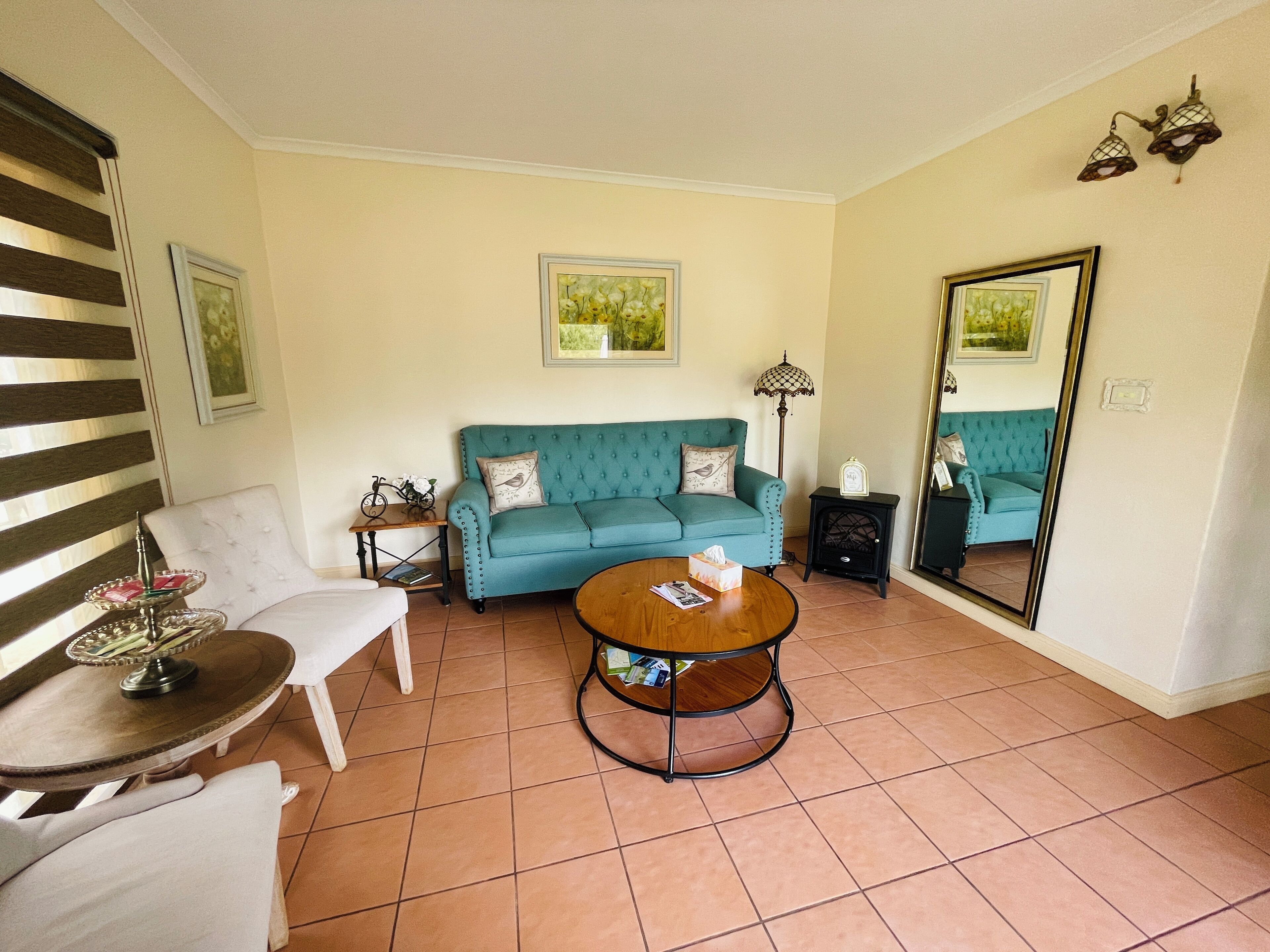 A living room with a teal sofa, a round coffee table, a white armchair, and a small side table with a lamp.
