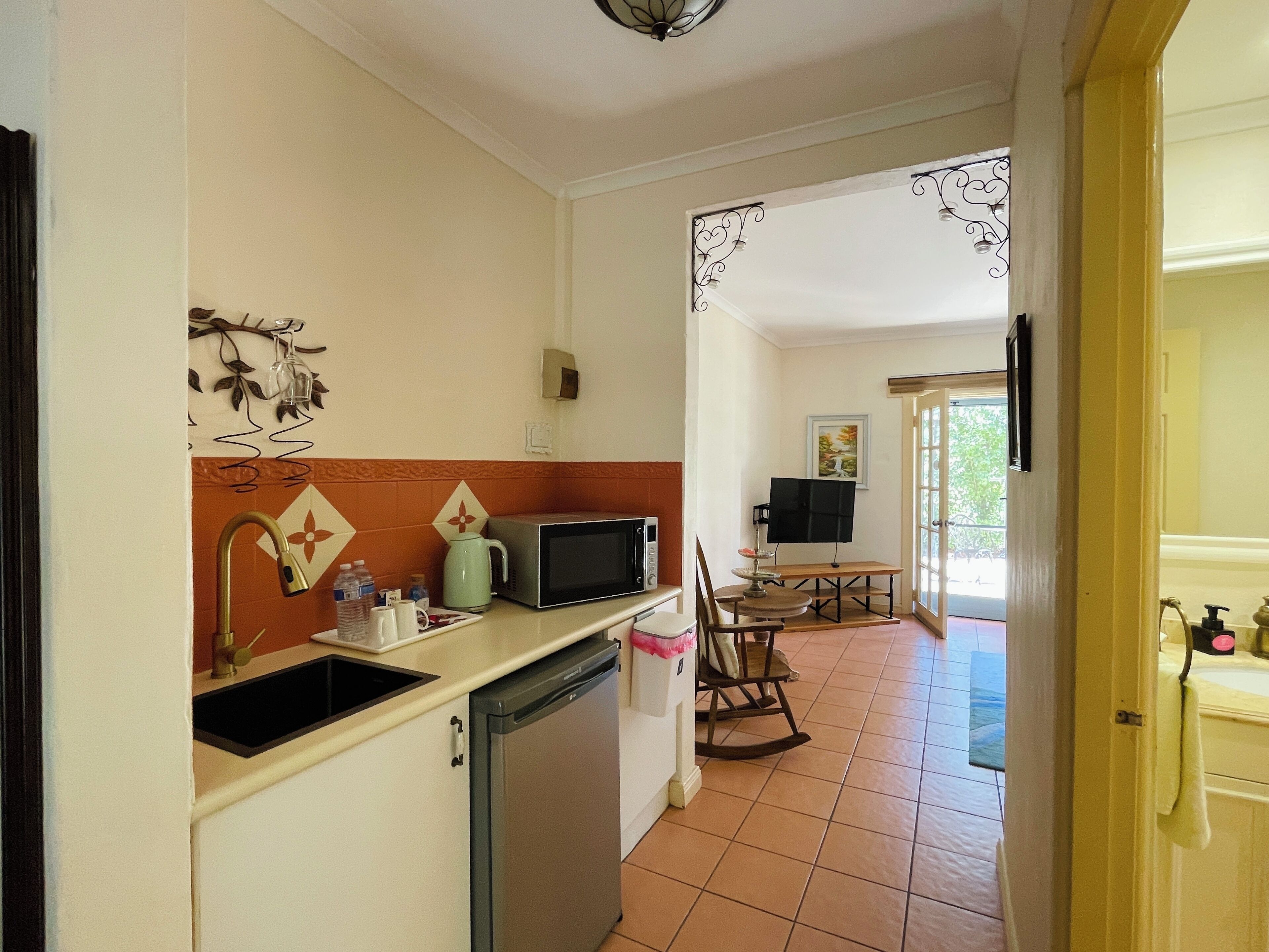 A compact kitchen with a sink, microwave, and refrigerator. A dining area with a table and chairs is visible in the background.