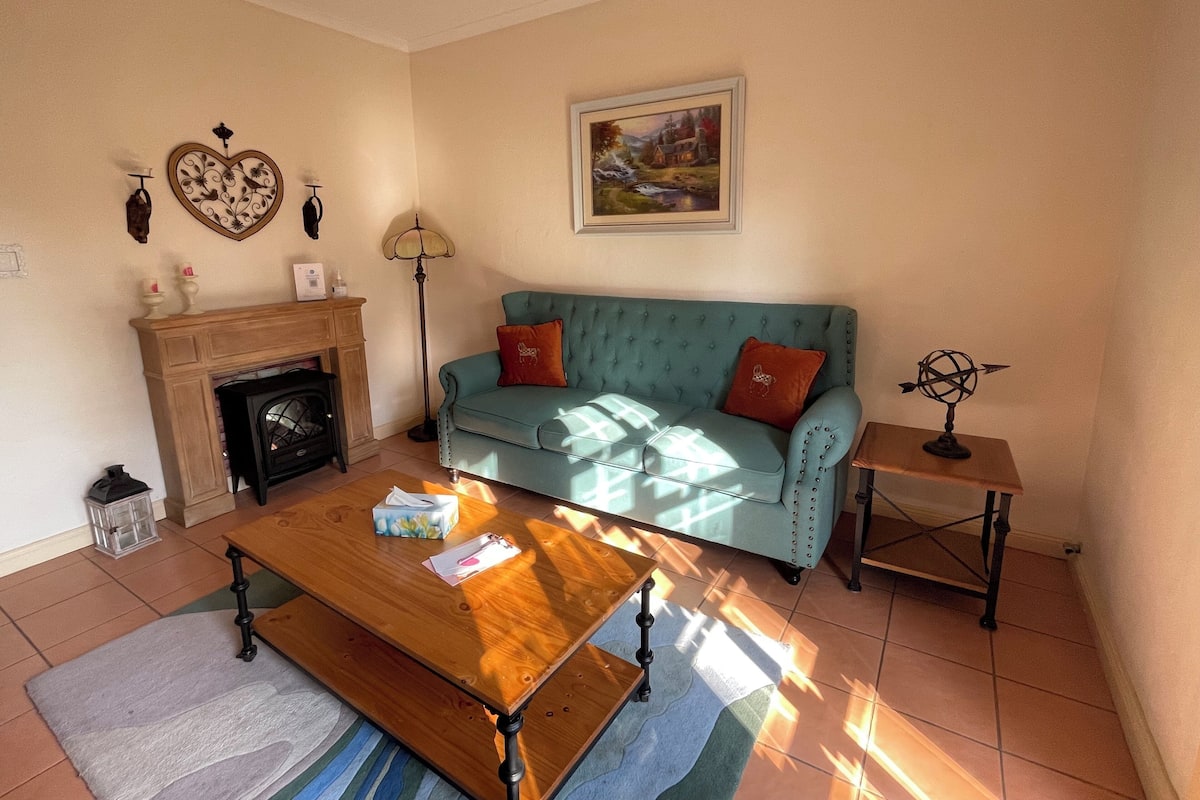 A cozy living room with a fireplace, a teal sofa with cushions, a wooden coffee table, and a framed painting on the wall.