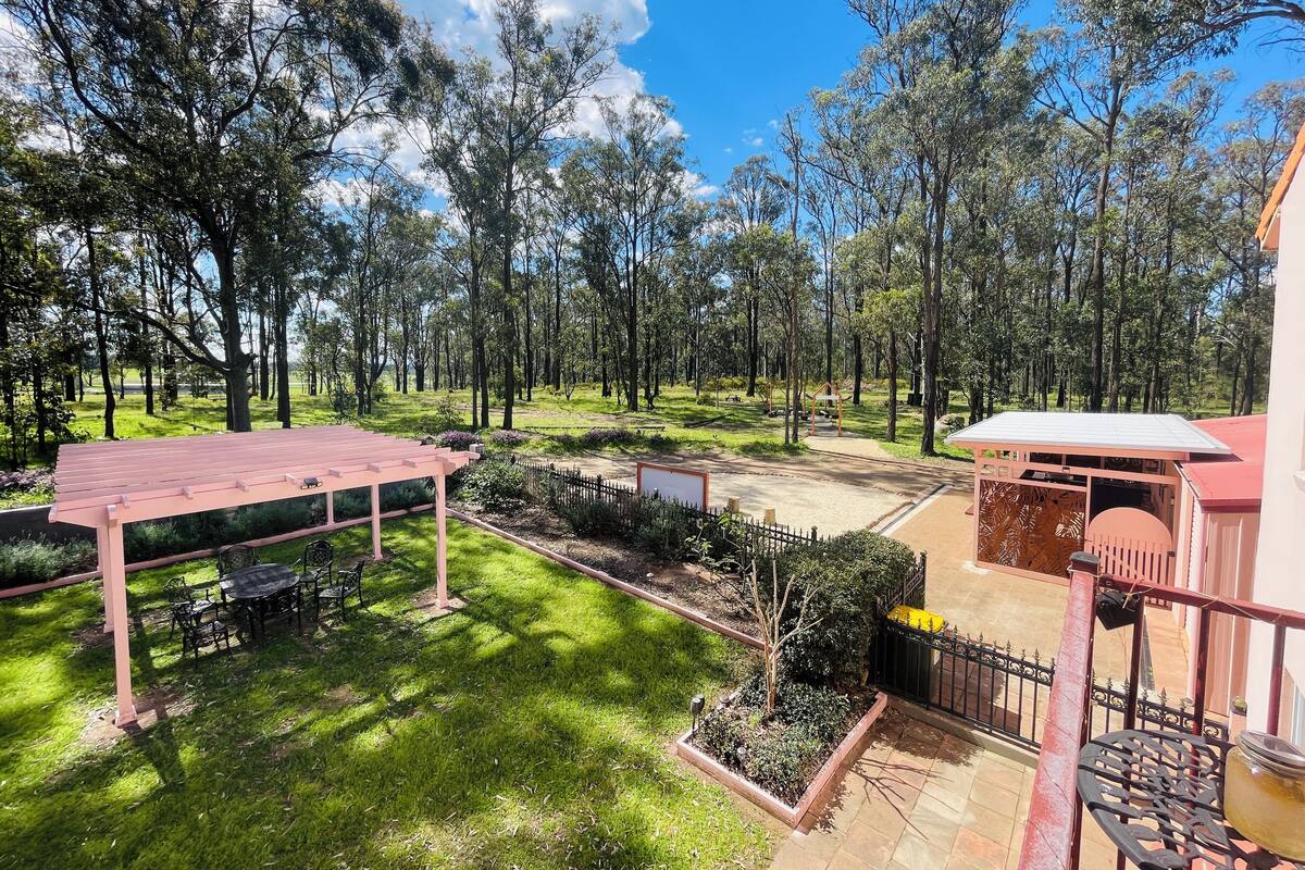 A spacious outdoor area with a wooden pergola, a covered seating area, and a view of a forested landscape.
