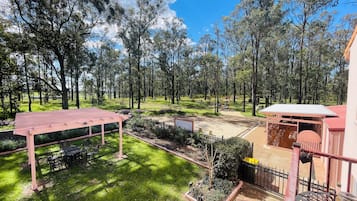 Amplio espacio al aire libre con una pérgola de madera, zona de estar cubierta y vistas a un paisaje boscoso.