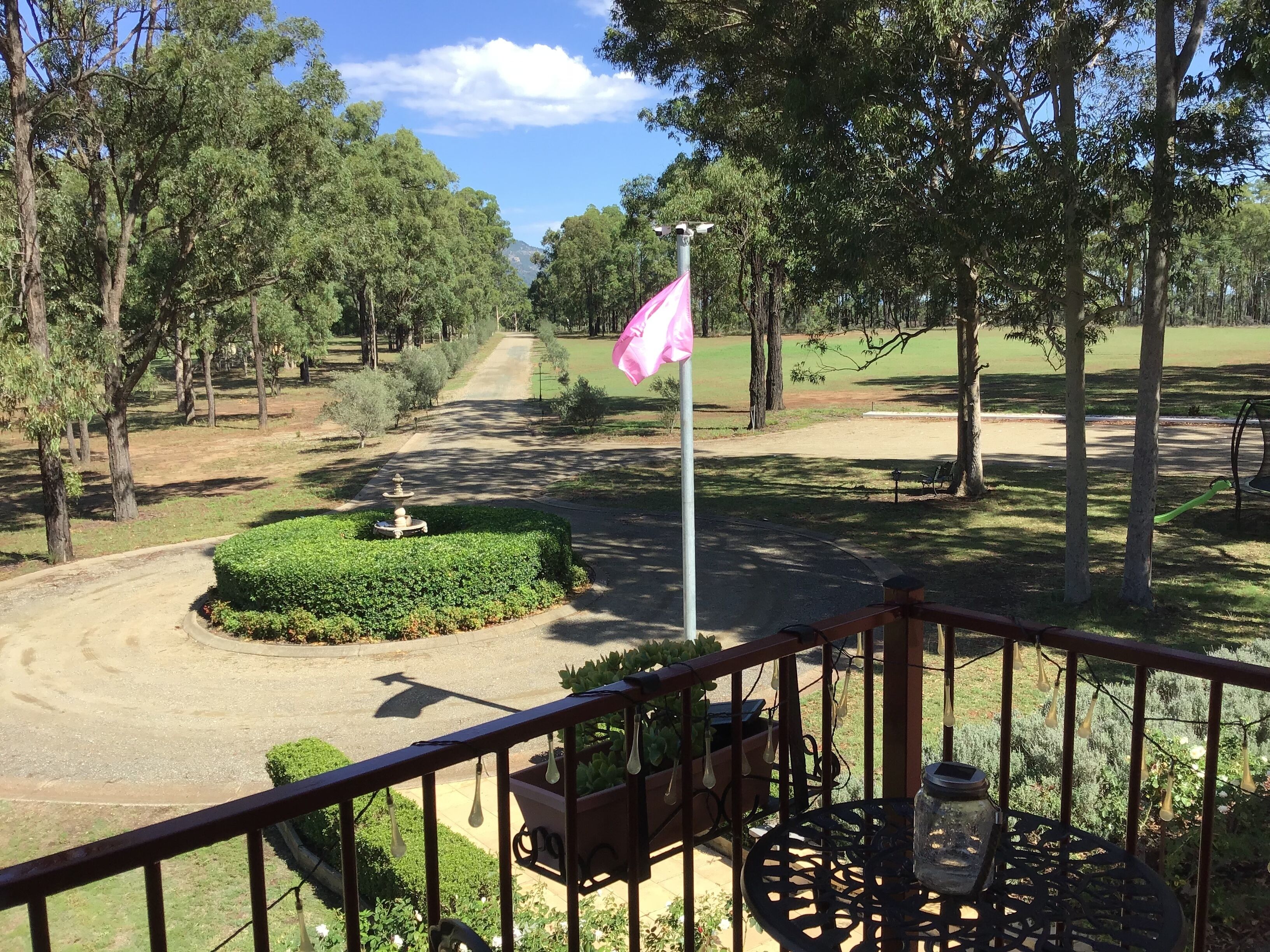 Un balcón con vista a un campo de golf, un asta con bandera y un pequeño jardín con fuente.