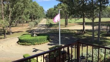 Un balcón con vista a un campo de golf, un asta con bandera y un pequeño jardín con fuente.