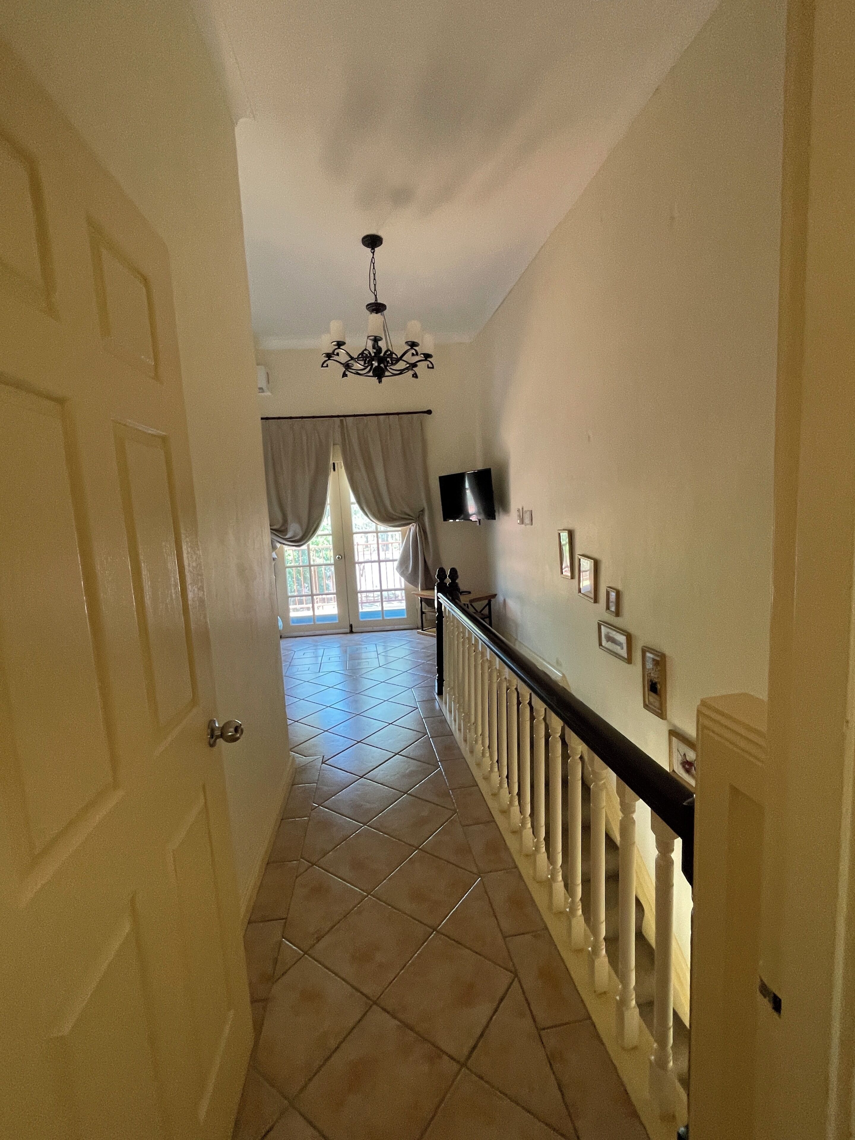 A hallway with a tiled floor, a chandelier, a staircase with a black railing, and a door on the left.