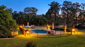 A swimming pool with a surrounding fence, lounge chairs, and a fountain. - Villa Provence (Pokolbin)