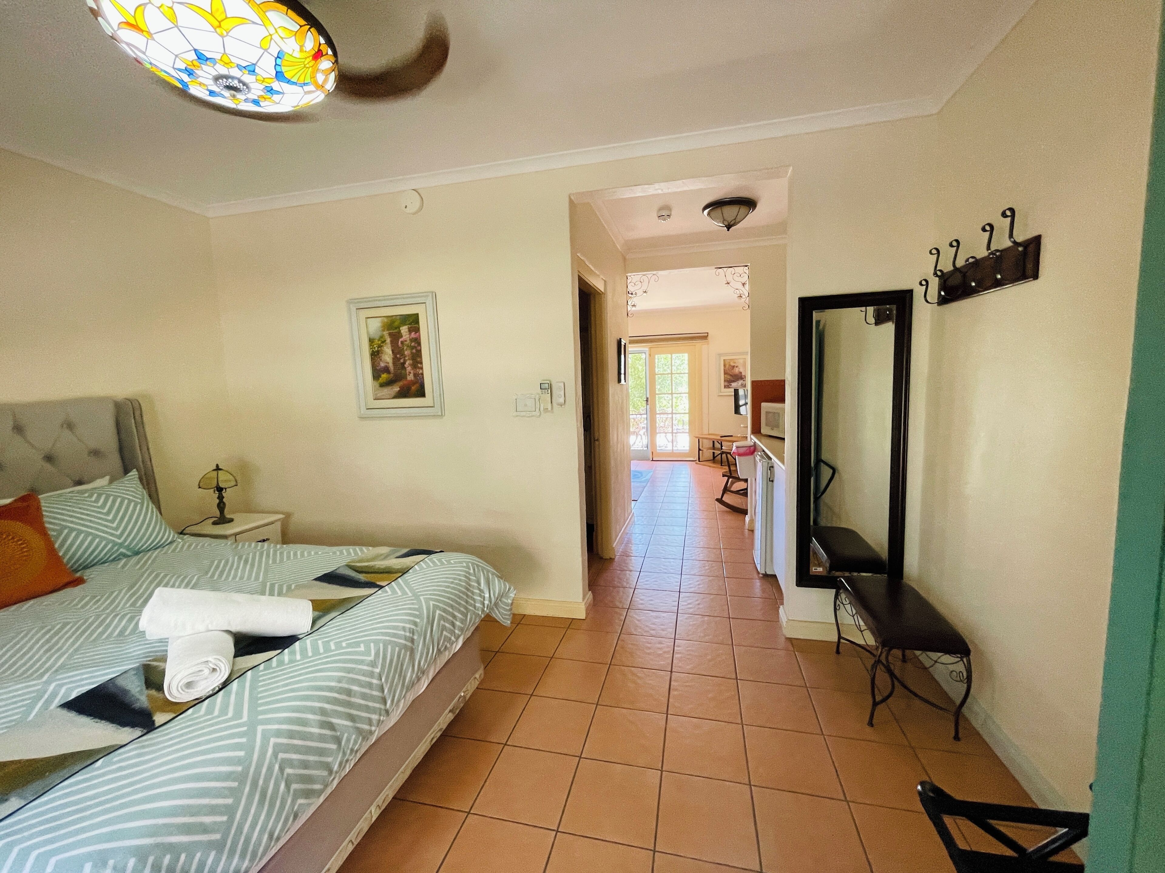 Un dormitorio con cama, mesita de noche, lámpara, cuadro enmarco y baño con espejo y lavabo.