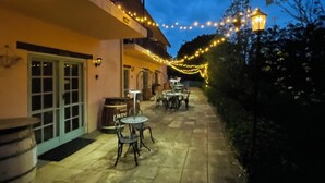 Ein möblierter Außenbereich mit Tischen und Stühlen, Lichterketten und einem Gebäude mit Balkon.