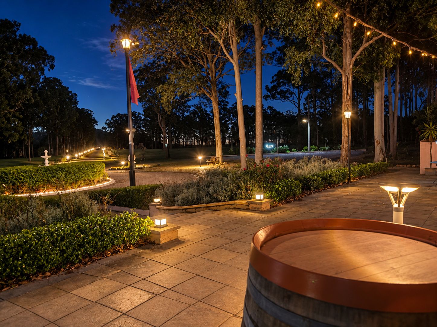 A well-lit outdoor area with a paved walkway, a wooden barrel, and a fountain.