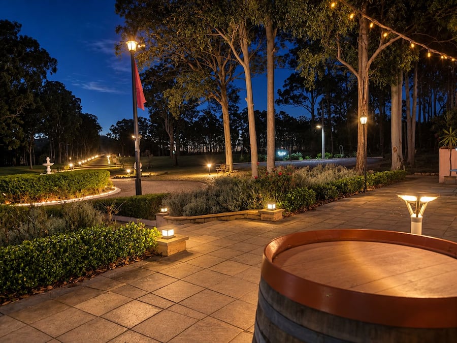 A well-lit outdoor area with a paved walkway, a wooden barrel, and a fountain.