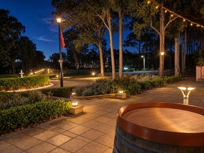 A well-lit outdoor area with a paved walkway, a wooden barrel, and a fountain. - Villa Provence (Pokolbin)