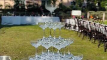 A table set with crystal glasses and silver pitchers, outdoors with a building and trees in the background.