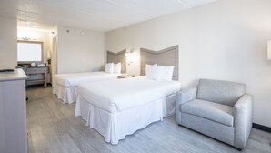 Habitación de hotel con dos camas, un escritorio, una silla y un baño visible a través de una puerta abierta.