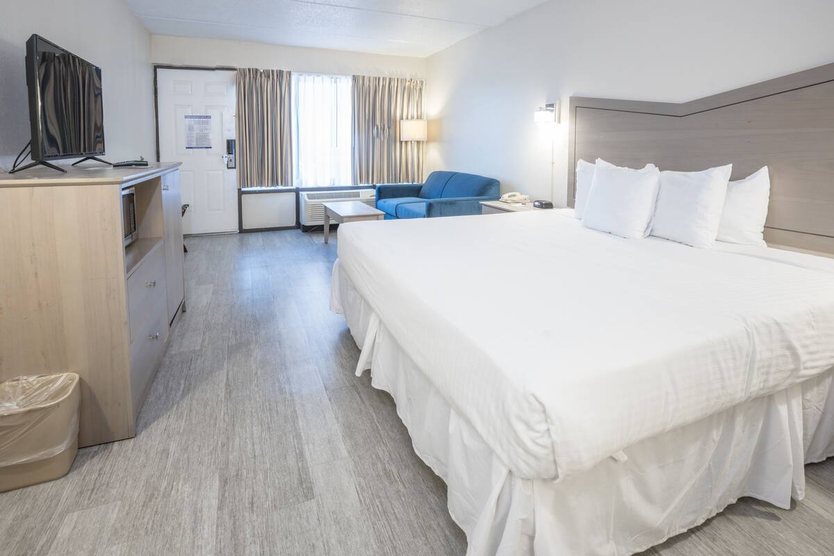 Ein Hotelzimmer mit einem großen Bett, einem Schreibtisch mit Computer, einem Sessel und einem Fernseher.