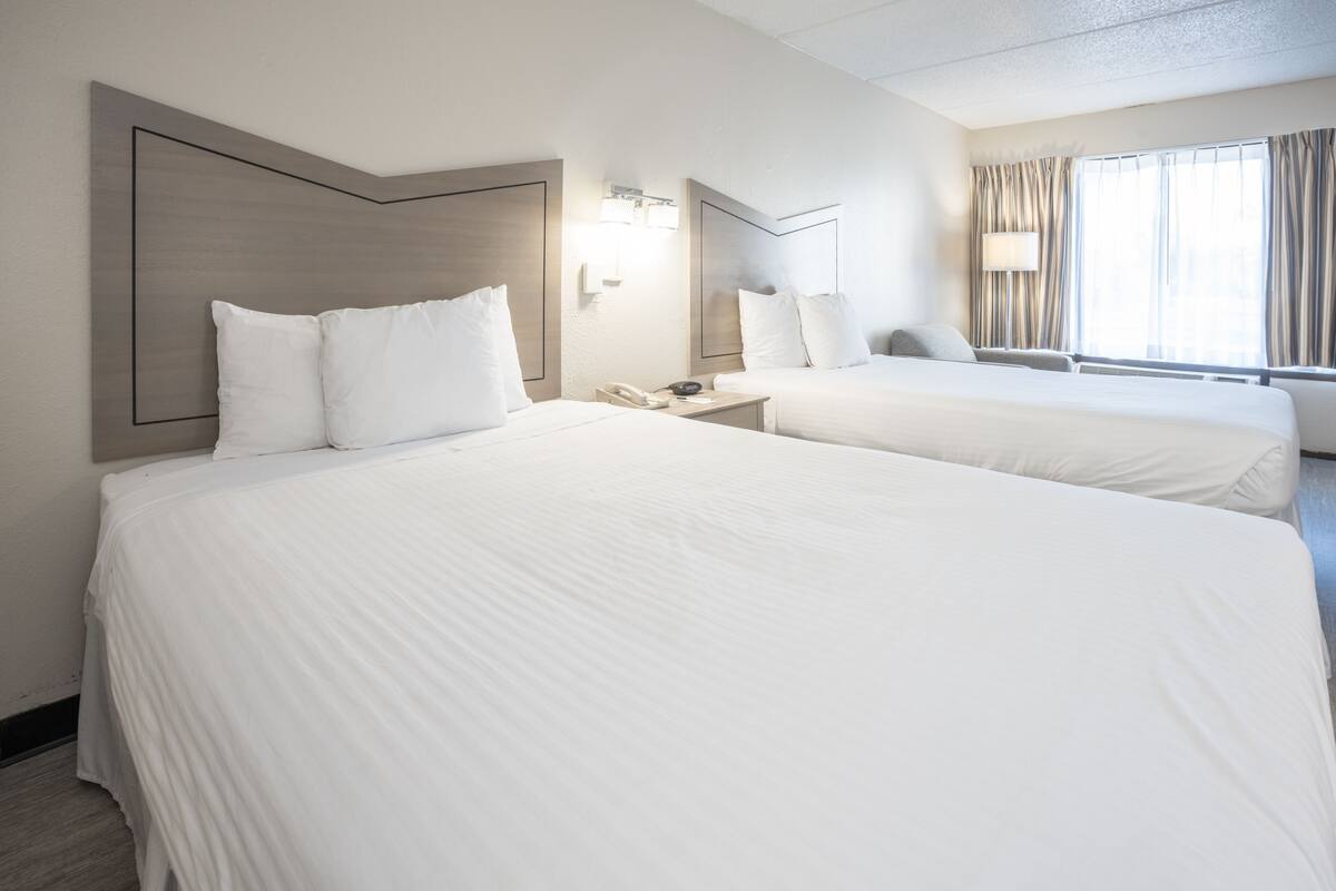 Ein Hotelzimmer mit zwei Betten, einem Nachttisch mit Lampe und einem Fenster mit Vorhängen.
