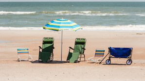 Una playa con cuatro sillas de playa y un paraguas azul.