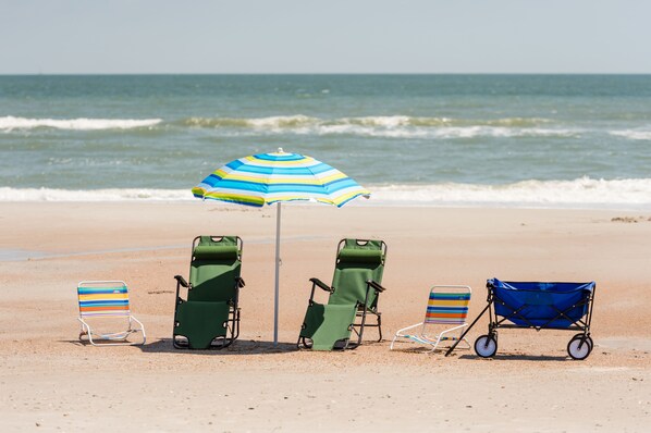 Ein Strand mit vier Liegestühlen und einem blauen Sonnenschirm.