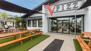 Un restaurante de pizza con terraza y un gran logotipo con la letra 'V'.