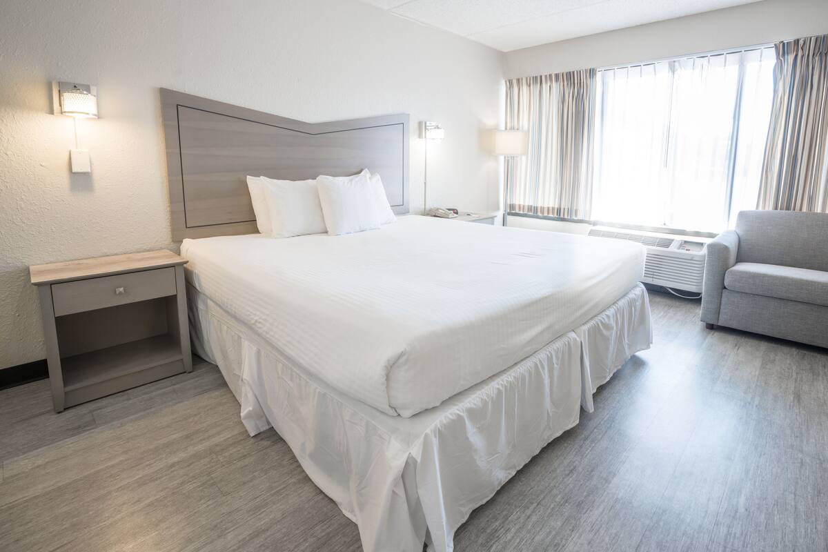 Ein Hotelzimmer mit einem großen Bett, Nachttischen, einem Sessel und einem Fenster mit Vorhängen.