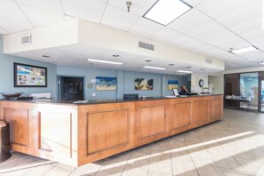 A reception area with a wooden counter, framed artwork on the walls, and a tiled floor. - Ocean Coast Hotel at the Beach (Fernandina Beach)