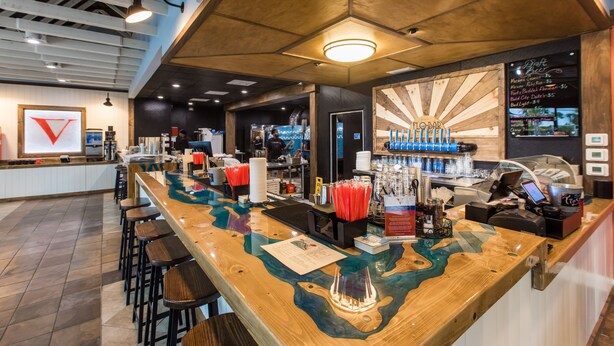 Una zona de bar con mostrador de madera, taburetes y una pizarra con el menú.