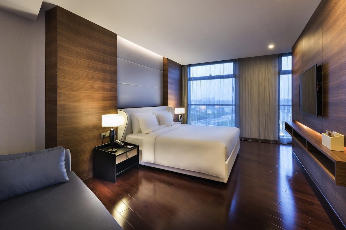Ein modernes Hotelzimmer mit einem großen Bett, Nachttischen, einem Flachbildfernseher und einem großen Fenster mit Blick auf die Stadt.
