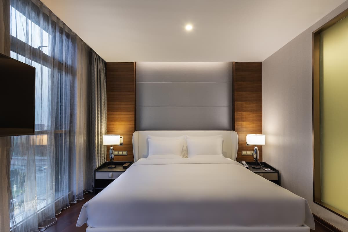 Ein Hotelzimmer mit einem großen Bett, zwei Nachttischen mit Lampen, einem Flachbildfernseher und transparenten Vorhängen.