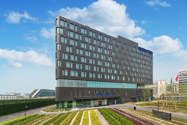 A modern hotel building with a flat roof, multiple windows, and a sign reading "NOVOTEL".