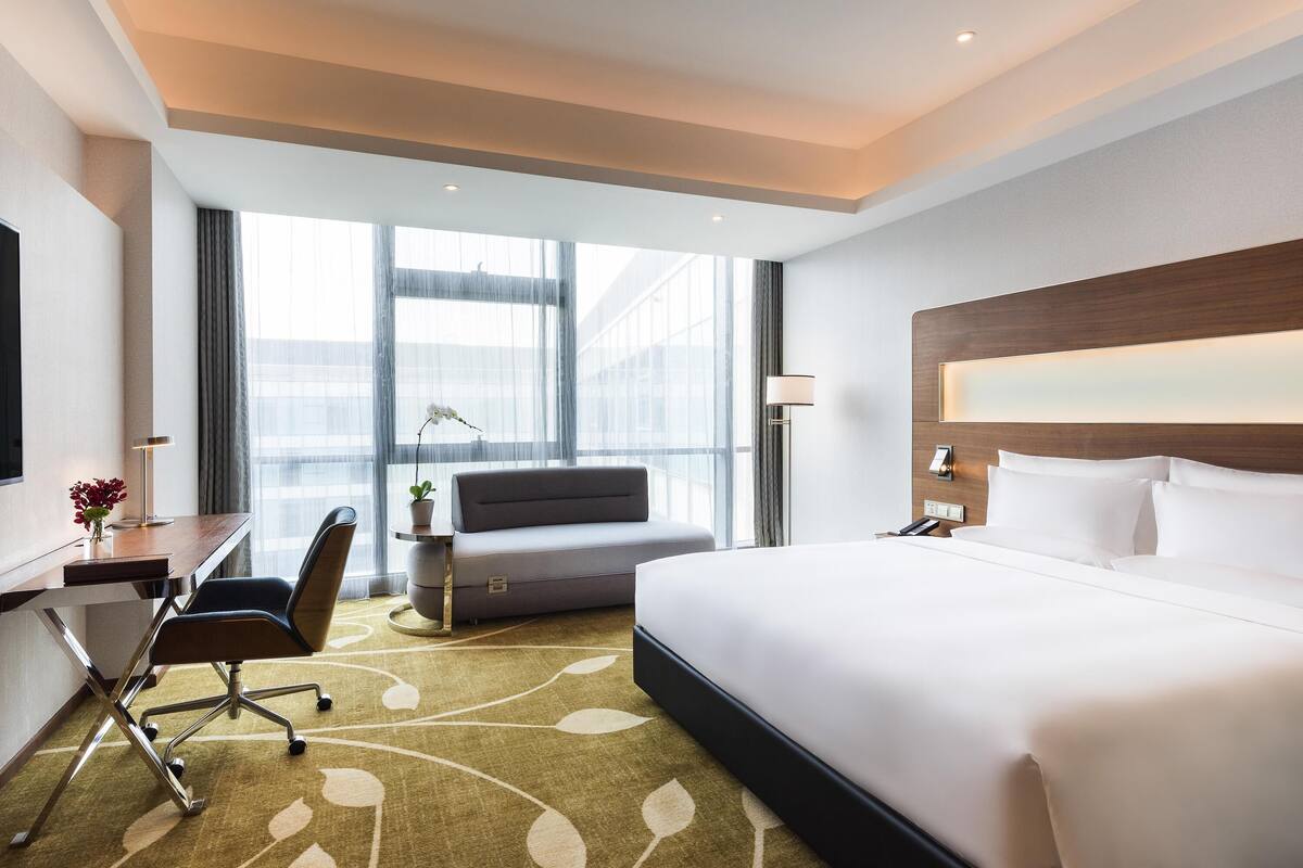 Ein Hotelzimmer mit Bett, Schreibtisch, Stuhl und großen Fenstern.