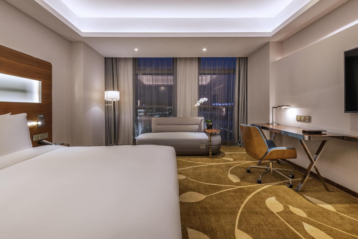 Ein Hotelzimmer mit Bett, Schreibtisch, Stuhl und einem großen Fenster mit Vorhängen.