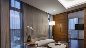 Een moderne hotelkamer met een bank, twee ronde tafels, een lamp en een groot raam met gordijnen.