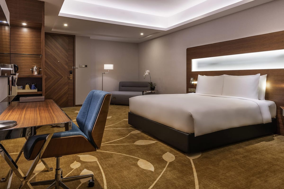 Une chambre d’hôtel moderne avec un grand lit, un bureau avec une chaise, une petite table et une table de chevet.