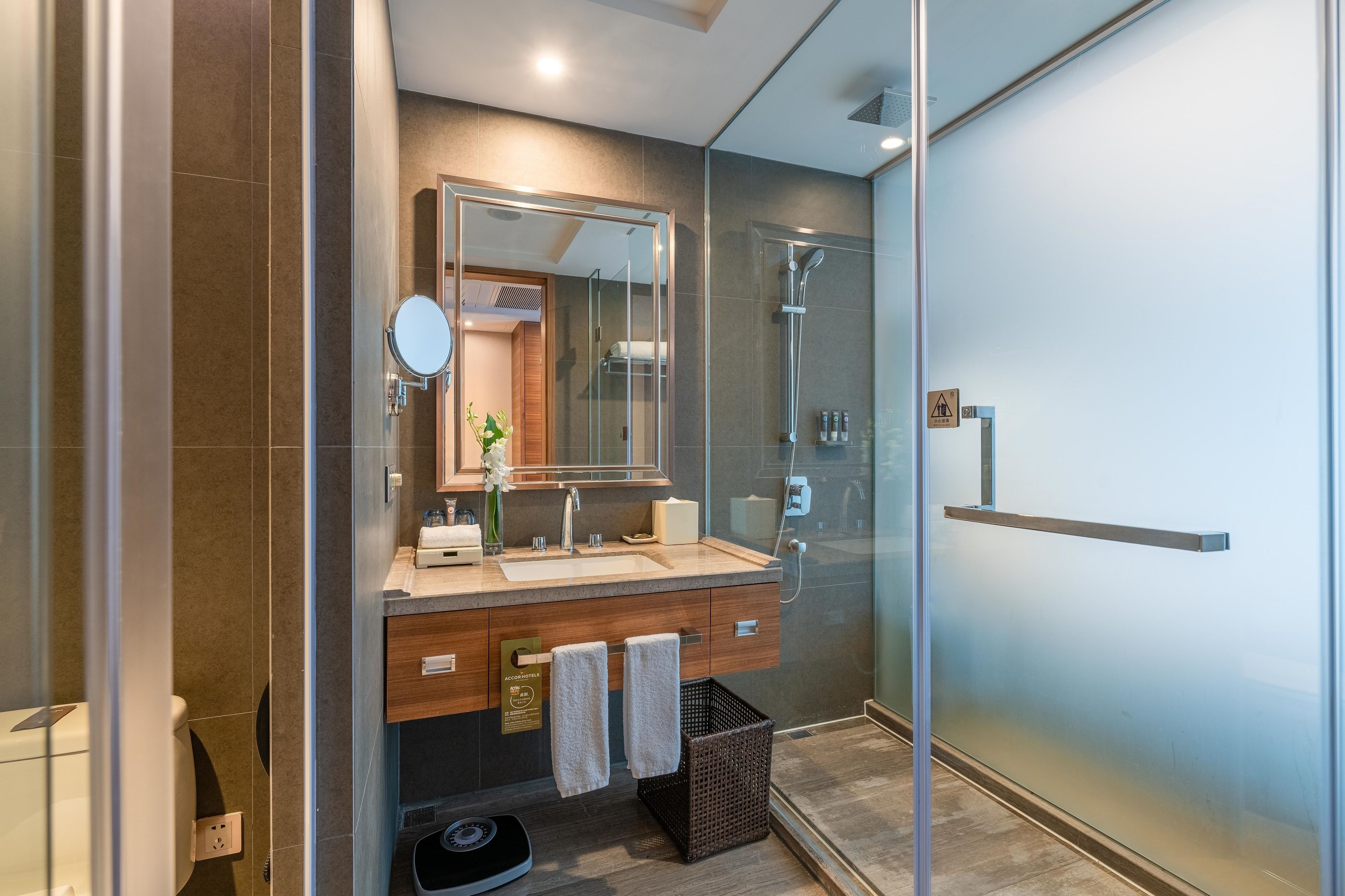 A modern bathroom with a glass shower enclosure, a wooden vanity, and a large mirror.