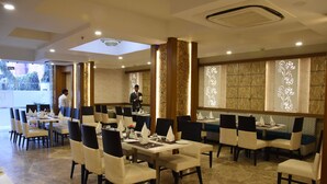 A restaurant with multiple dining tables and chairs, a chandelier, and decorative wall panels. - Meadows (Varanasi)