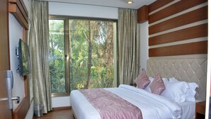 A bedroom with a large window, a bed with white and pink bedding, and a wooden headboard. - Meadows (Varanasi)