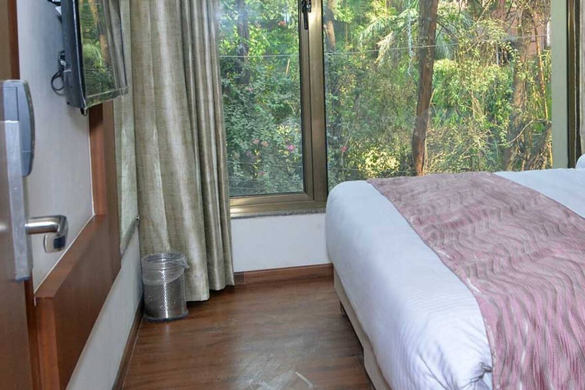 A neatly made bed with a striped bedspread and pillows, a tufted headboard, and a window with curtains.