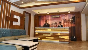 A reception area with a wooden reception desk, a blue sofa, and a tiled floor. - Meadows (Varanasi)