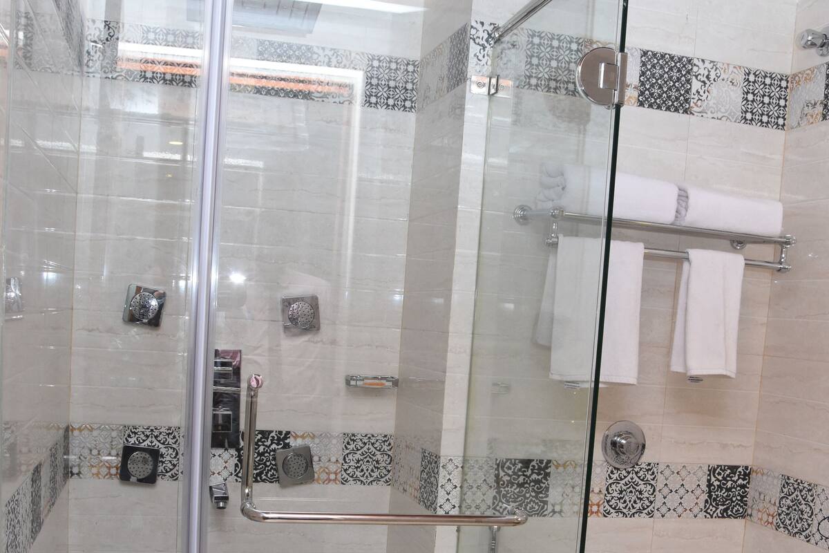 A glass-enclosed shower stall with a white toilet and a blue bucket.