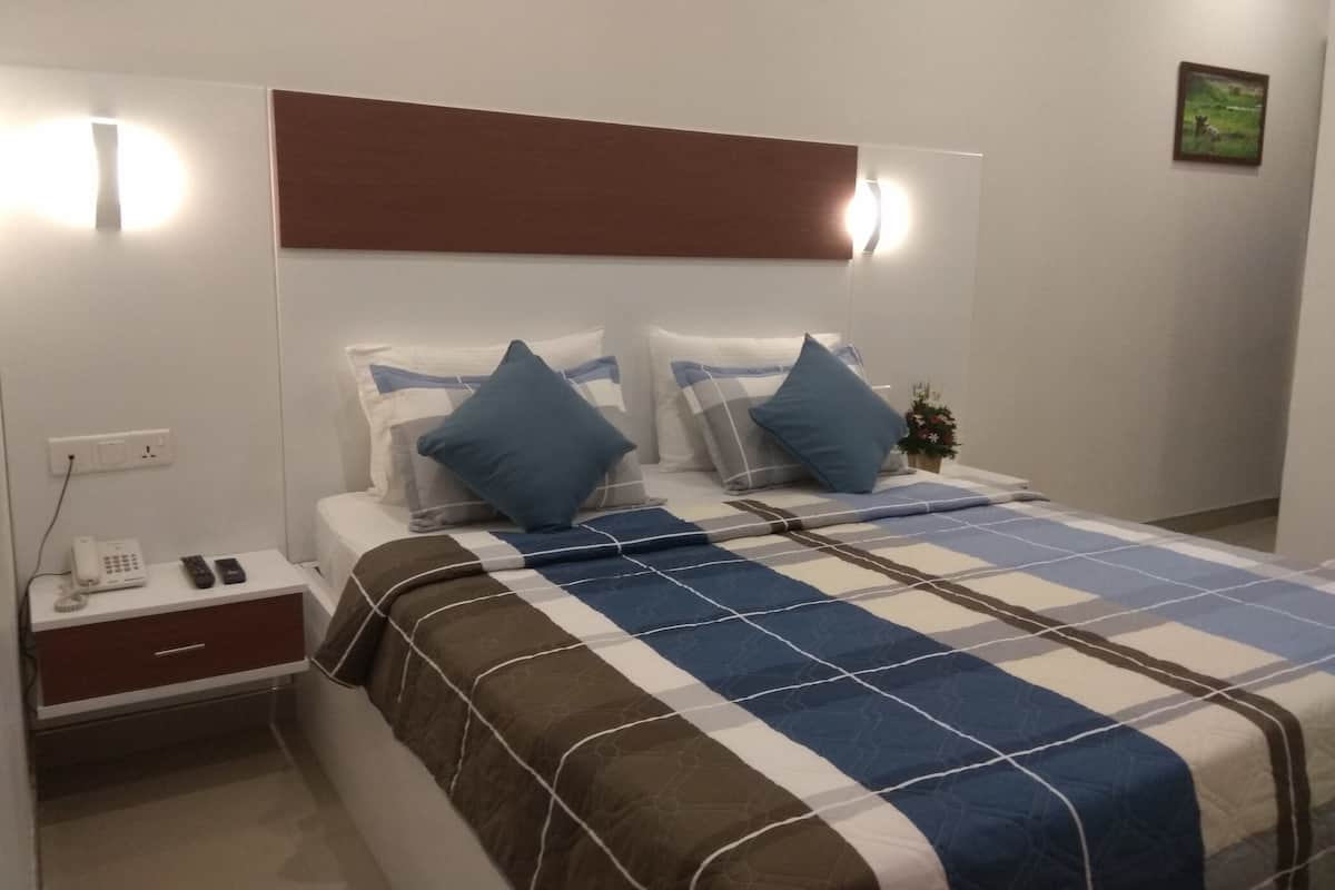 Una cama bien hecha con una colcha a cuadros, dos almohadas, una mesita de noche con un teléfono y una planta pequeña en la mesita.