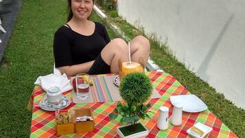 Iemand zit aan een buitentafel met een kleurrijke geruit tafelkleed, een kleine bloempot, een theepot, een zoutvaatje en een menukaart.