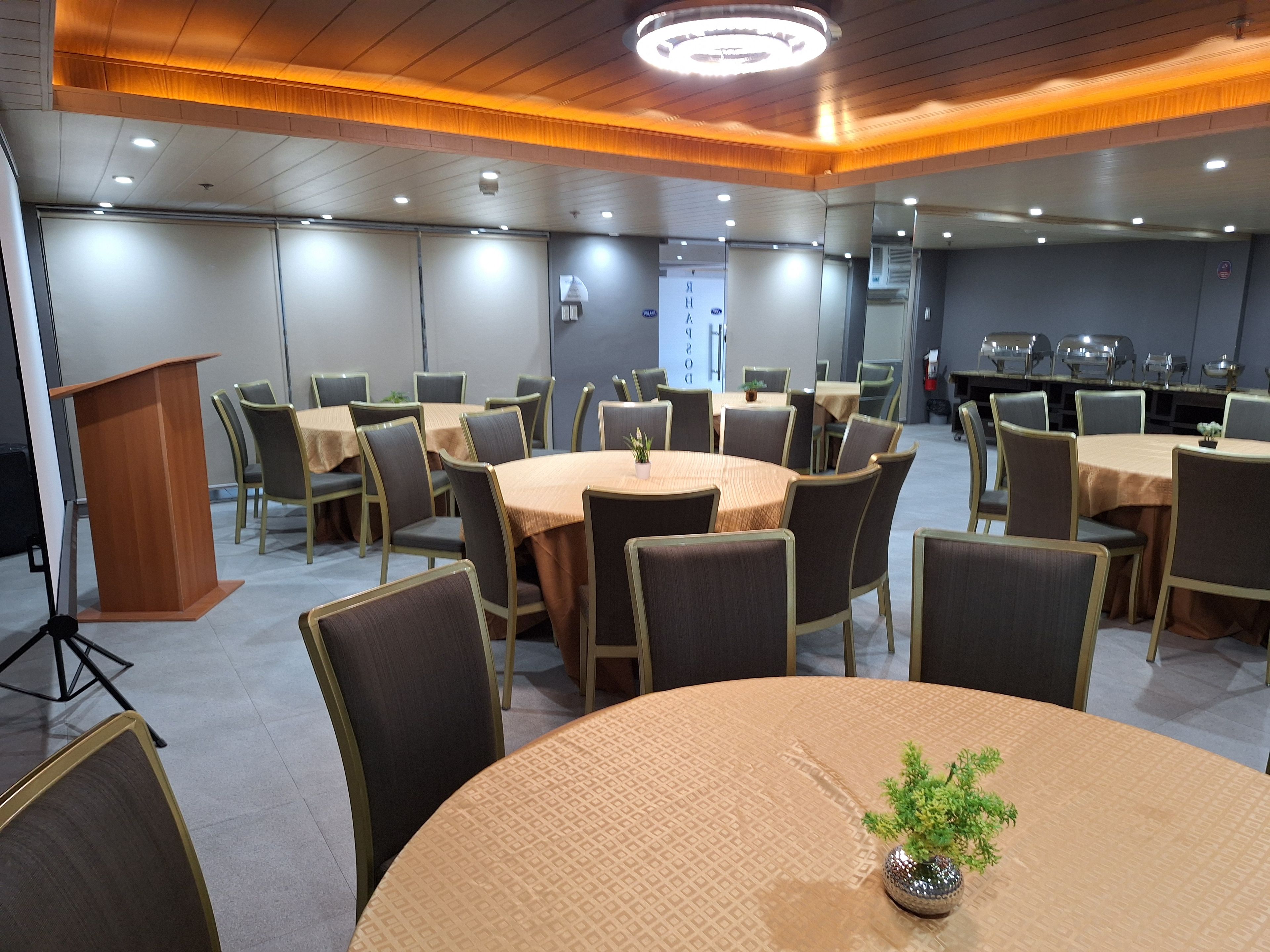 A conference room with multiple tables and chairs, a podium, and a large window.