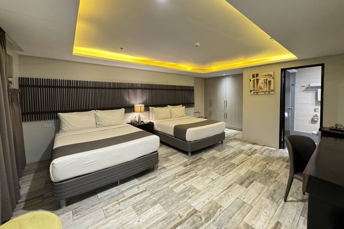 Quarto de hotel moderno com duas camas, uma escrivaninha e uma cadeira.