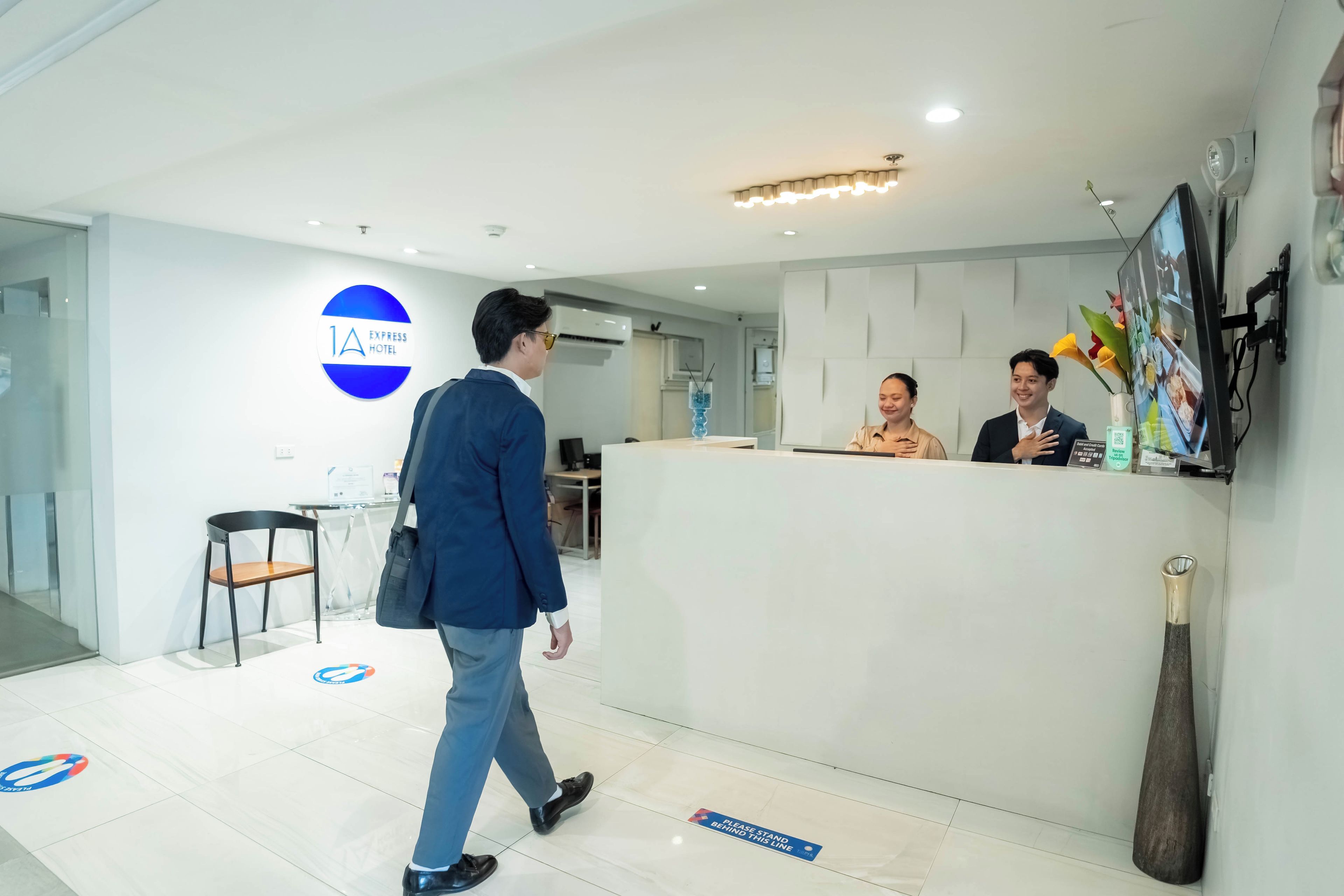 A hotel reception area with a modern design, a reception desk, and a digital screen displaying information.