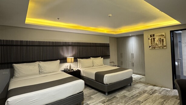 A modern hotel room with two beds, a wooden floor, a ceiling light, and a wall-mounted cabinet. - 1A Express Hotel (Cagayan de Oro)