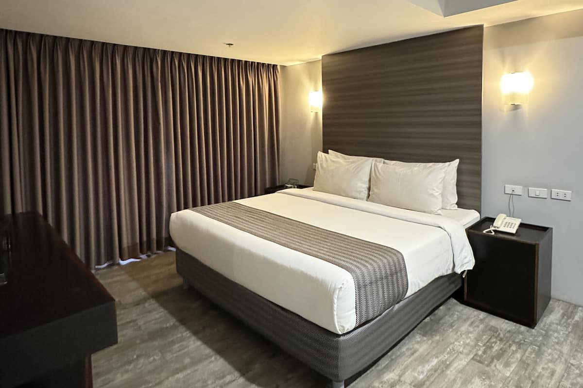 Quarto de hotel com uma cama grande, mesa de cabeceira com telefone e escrivaninha com cadeira.