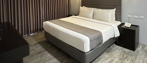 Una habitación de hotel con una cama grande, una mesita de noche con teléfono y un escritorio con una silla.