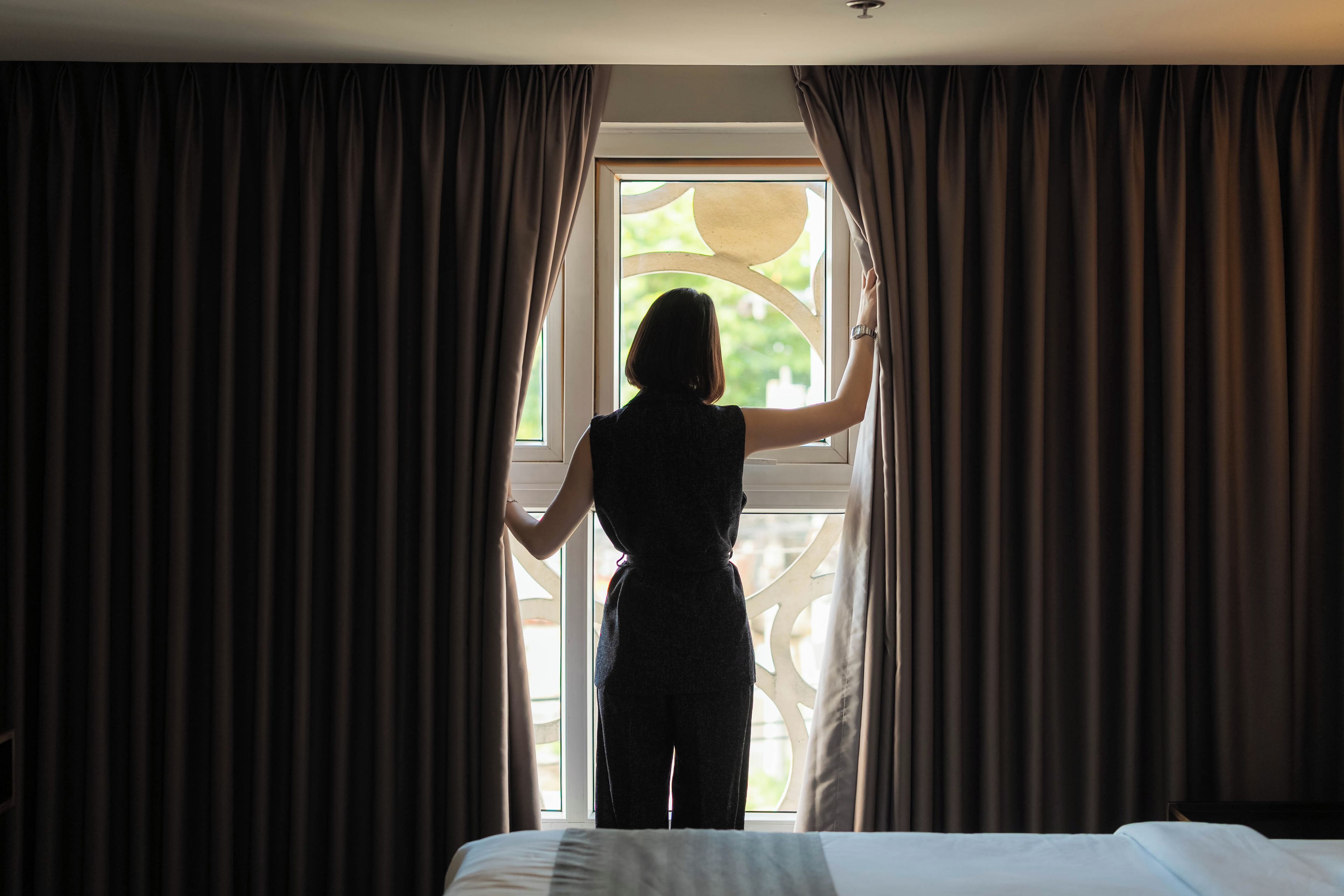 Uma pessoa em frente a uma janela com cortinas, olhando para o exterior.