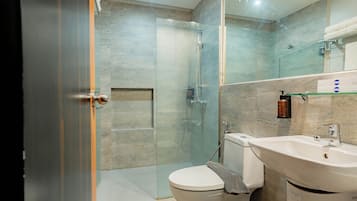 A modern bathroom with a glass shower enclosure, a white toilet, and a sink with a soap dispenser.